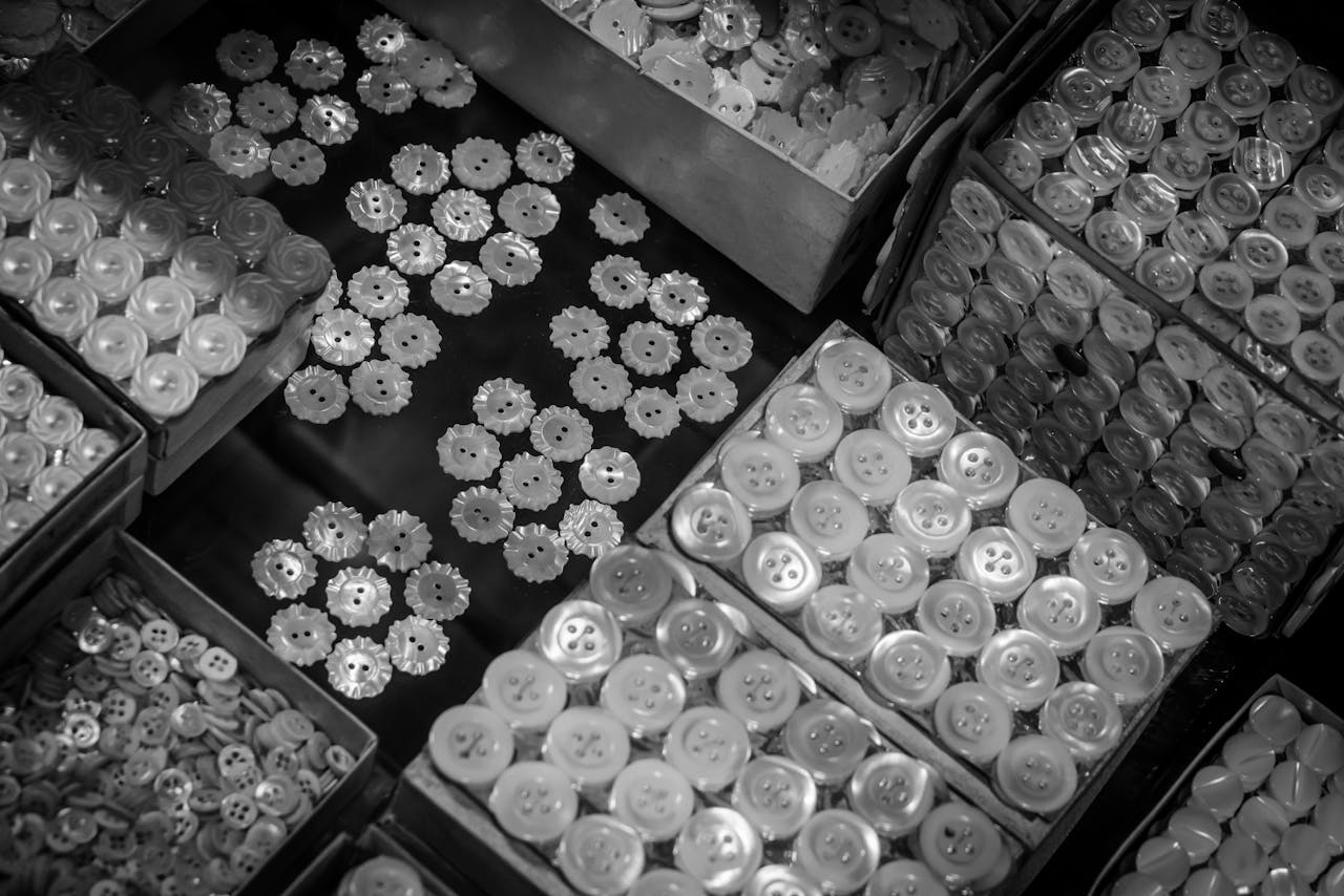 A vintage black and white photo displaying assorted buttons neatly organized in boxes.