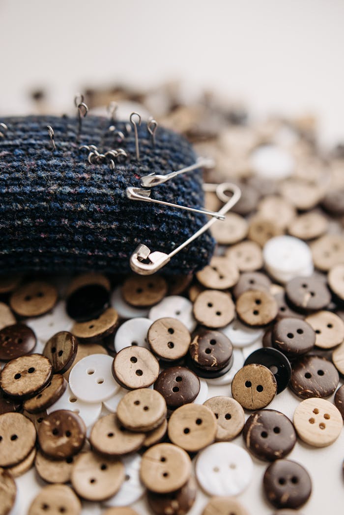 Close-up of sewing materials including a pincushion with safety pins and assorted buttons.
