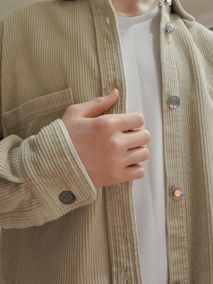 Person adjusting a beige corduroy jacket with metal buttons, showcases texture detail.