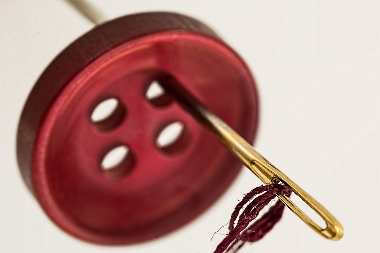 Macro photograph of a needle threading red thread through a brown button.
